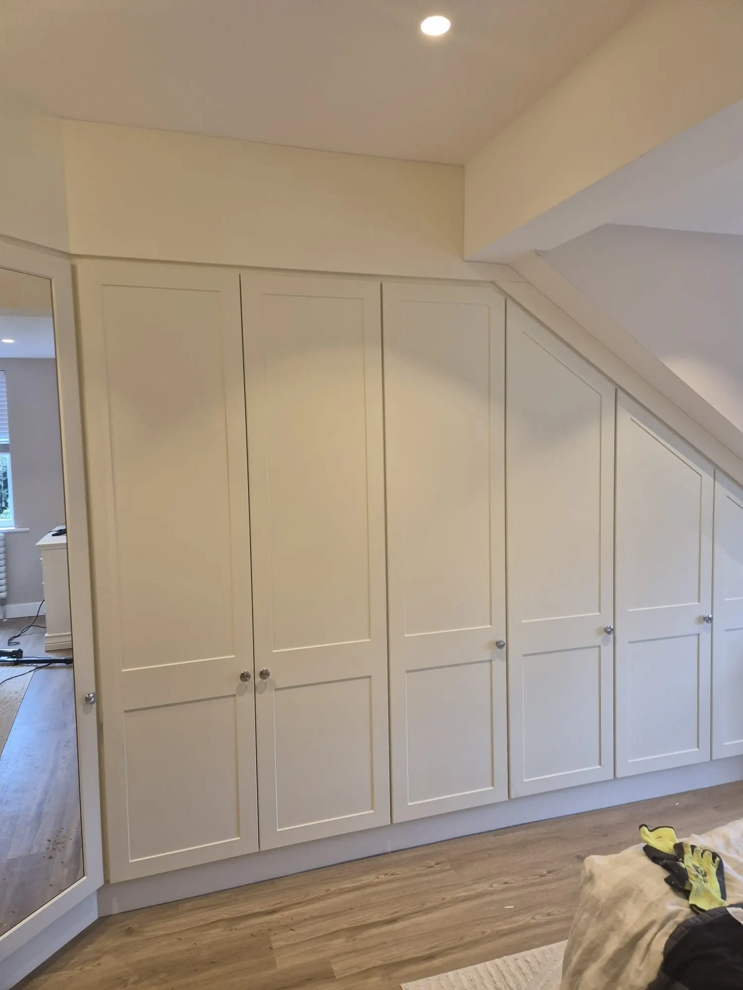 Wall-to-wall fitted wardrobes running under a sloping roof into a mirrored corner, fitted by CKC